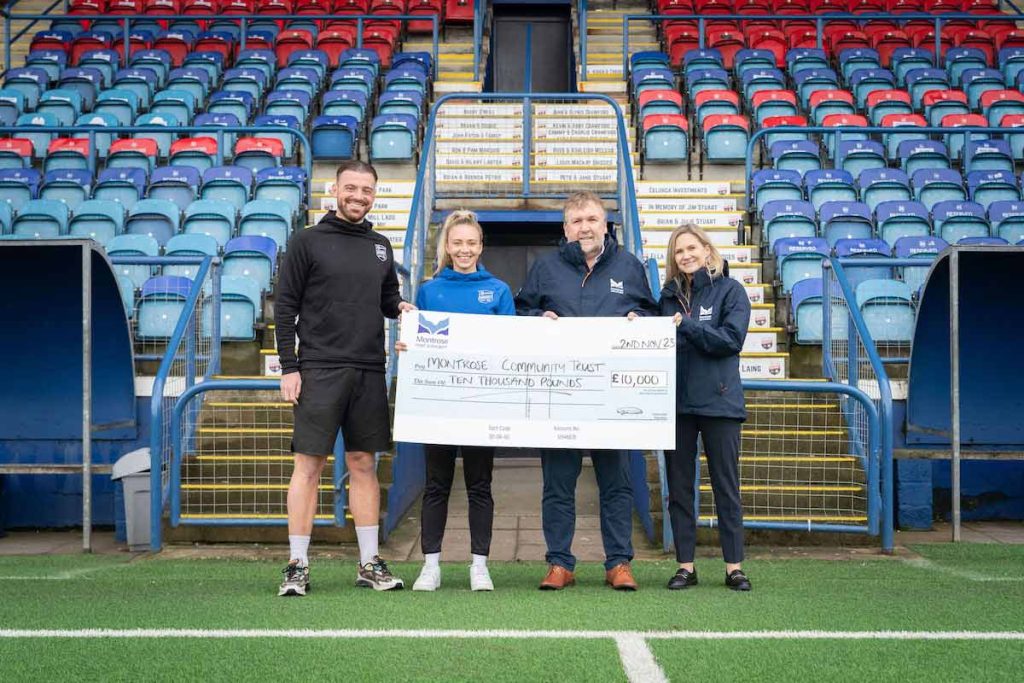 Kerr Waddell and Eilidh Reid from Montrose Community Trust holding a large cheque for £10,000 from Ann Rooney and Tom Hutchison at Montrose Port Authority on the side of the football pitch at Links Park Stadium in Montrose, Angus.