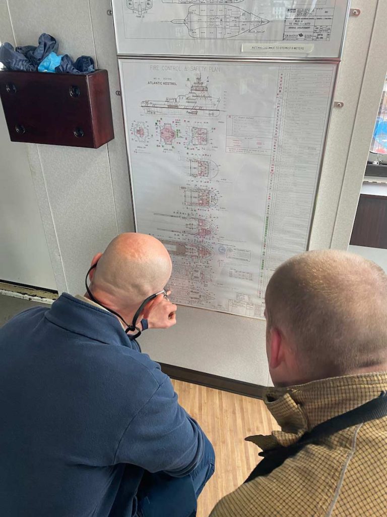 two men look at the layout plans of a vessel on the wall during a safety exercise at Montrose Port Authority