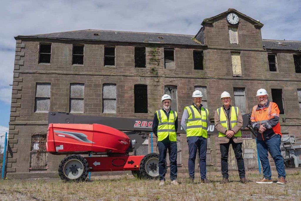 Brandon Bryant and Craig Bruce from Pert Bruce Construction, Garry Adam from Adam & Gordon Architects, and Tom Hutchison, CEO of MPA all standing in front of Customs House in Montrose next to a manitou and all wearing high-vis and hard hats. 