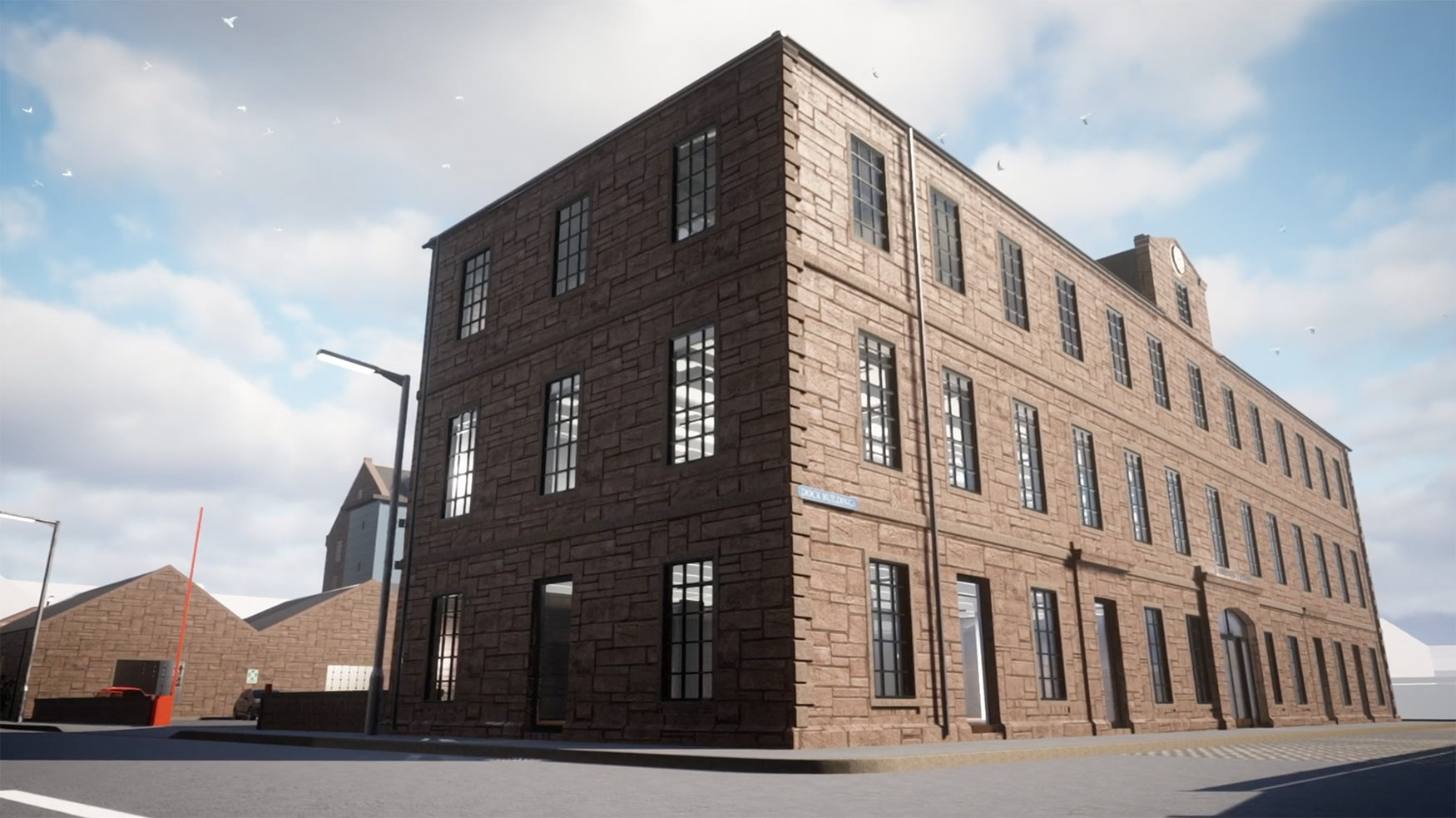 A large, three-storey brick building with many windows stands on a corner under a partly cloudy sky. The street and pavement are empty, and smaller industrial buildings are visible in the background.